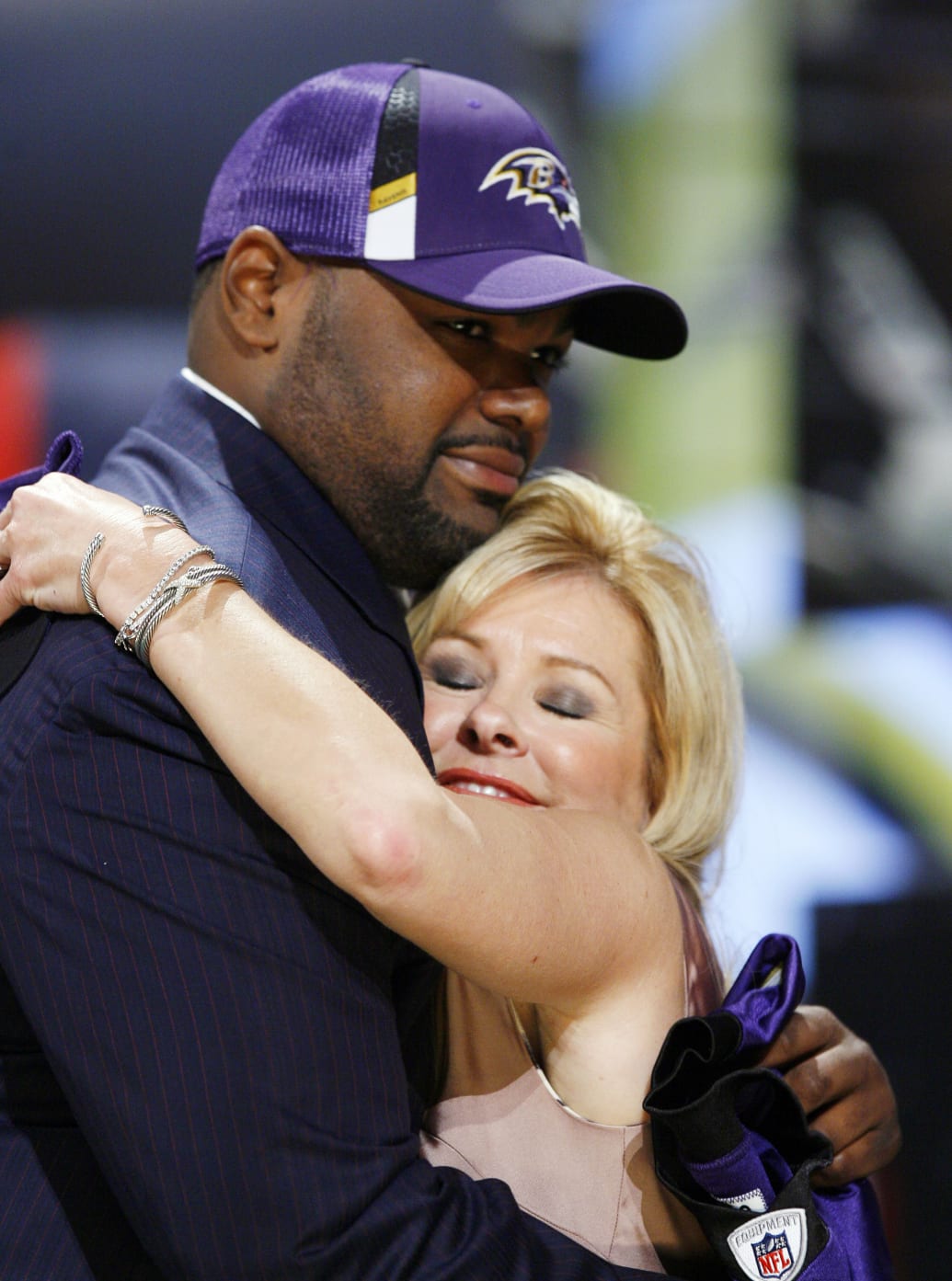 Michael Oher embraces Leigh Anne Tuohy as he wears a suit and Baltimore Ravens cap after being drafted in 2009.
