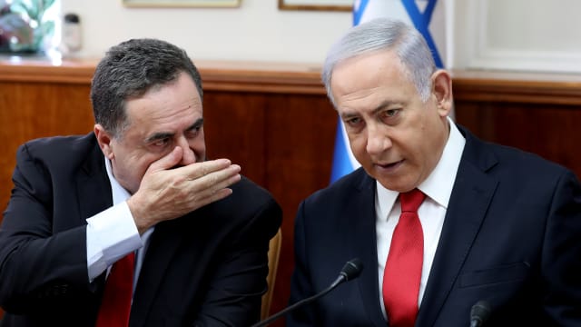 Israeli Prime Minister Benjamin Netanyahu listens to Foreign Minister Israel Katz who has his hand over his mouth.