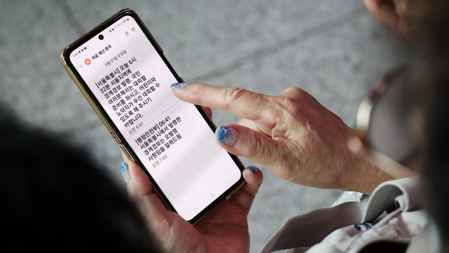 A woman looks at her cellphone with an emergency evacuation message while watching a TV broadcasting a news report on North Korea firing what it called a space satellite toward the south, in Seoul, South Korea, May 31, 2023.  