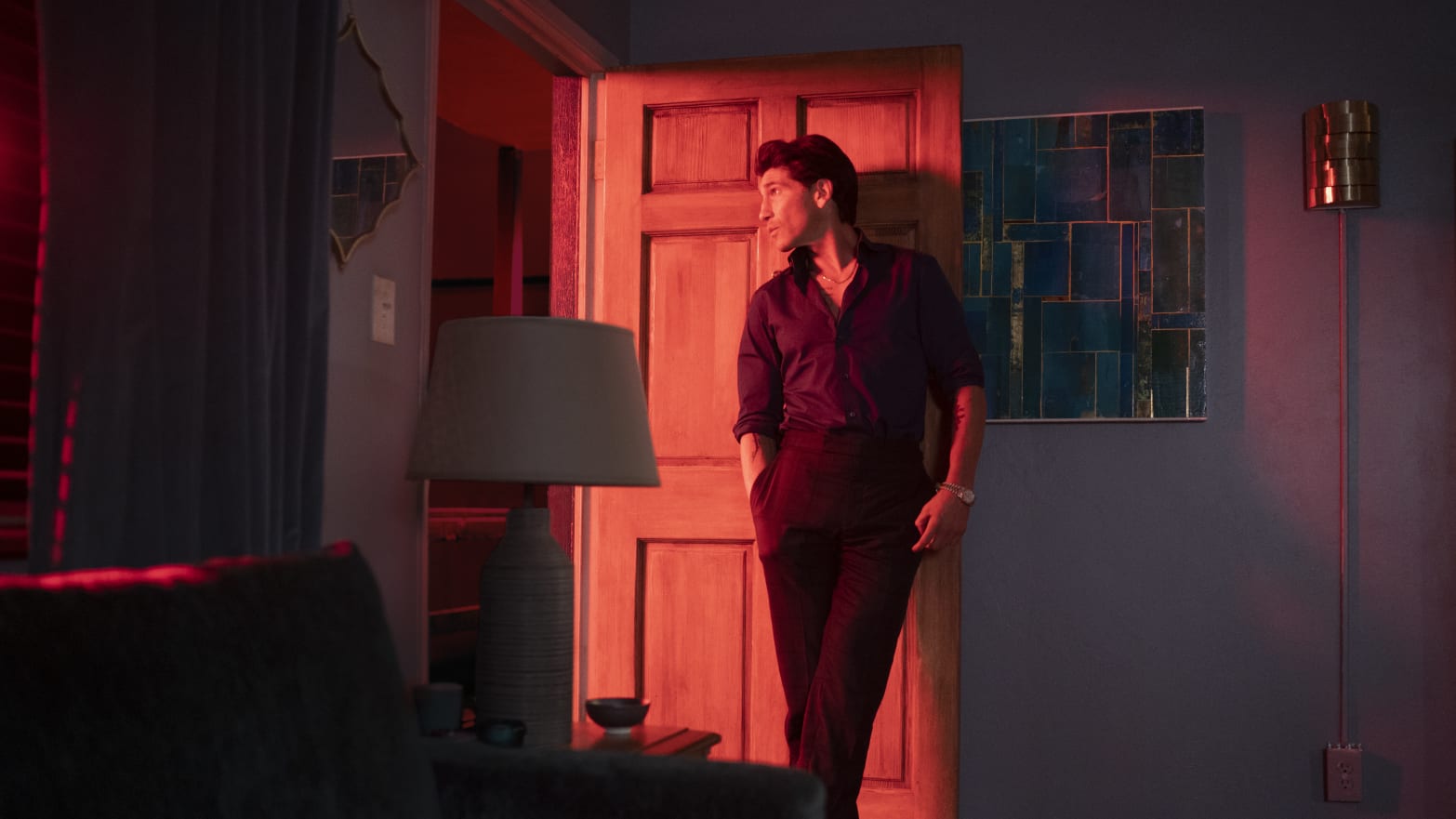 A man stands against a wall in a red-lit room.