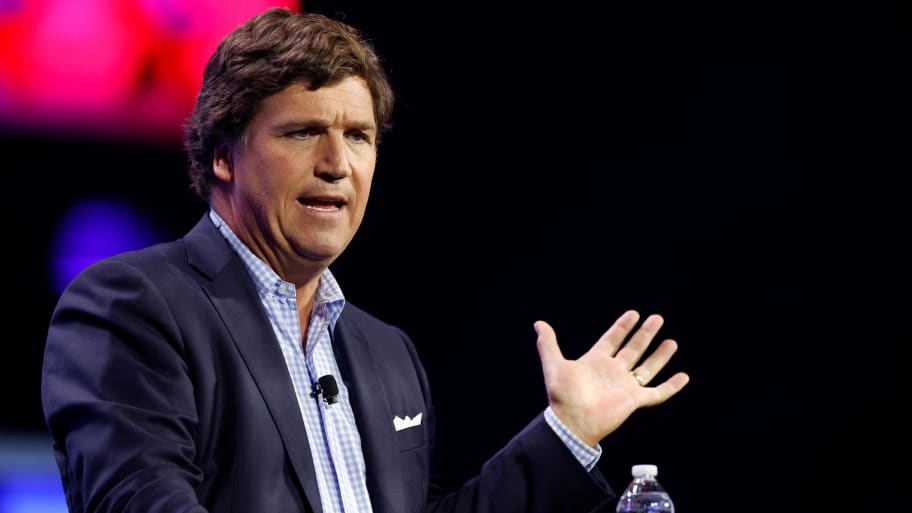 Tucker Carlson speaks with a hand raised on stage.