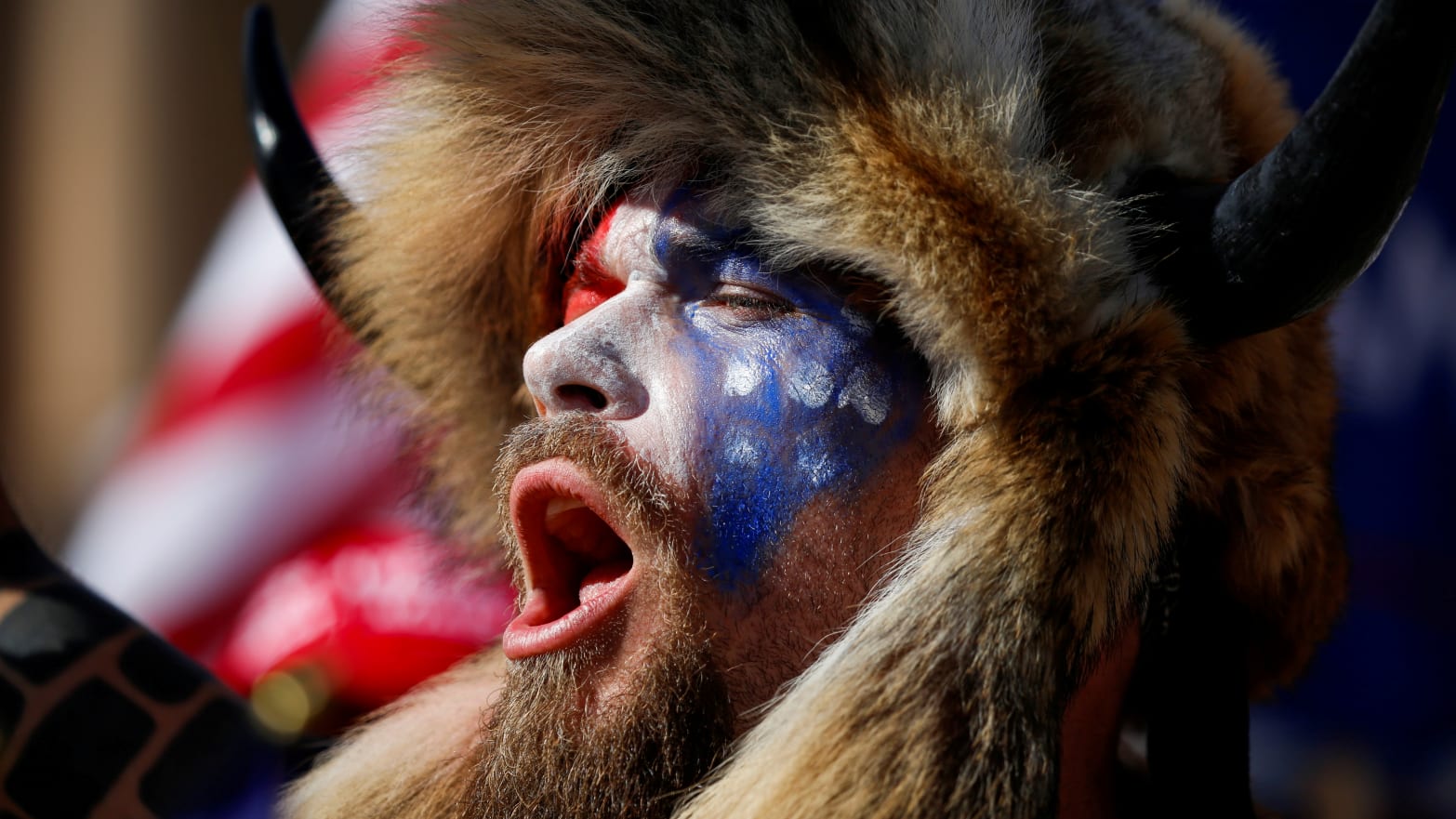Jacob Chansley, wearing face paint and a fur hat, screams during a protest.
