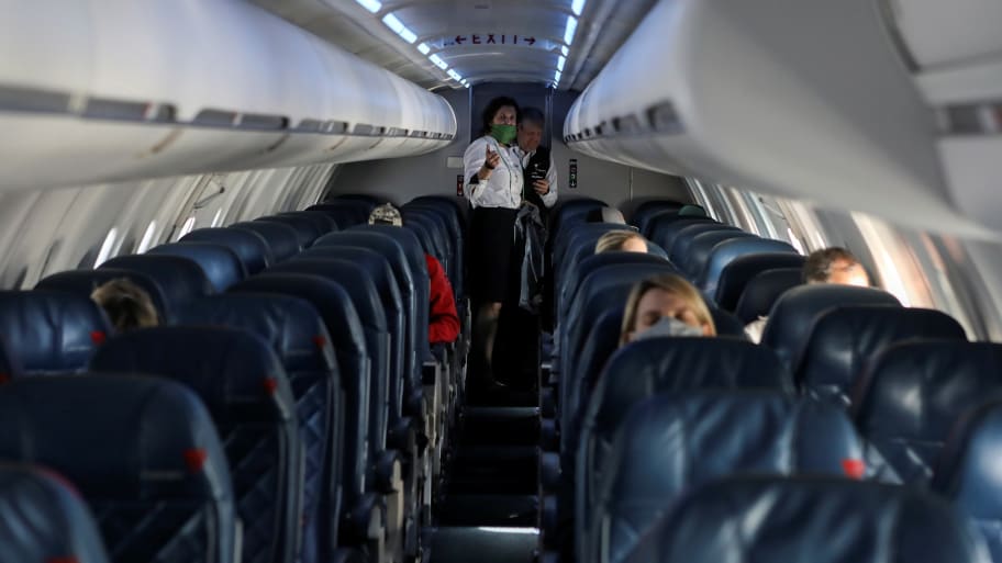 Flight attendants talk in a cabin while passengers sit in their seats
