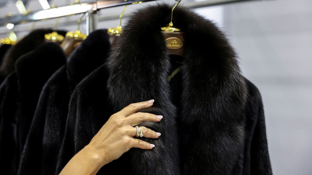 A worker holds a fur coat in a showroom.