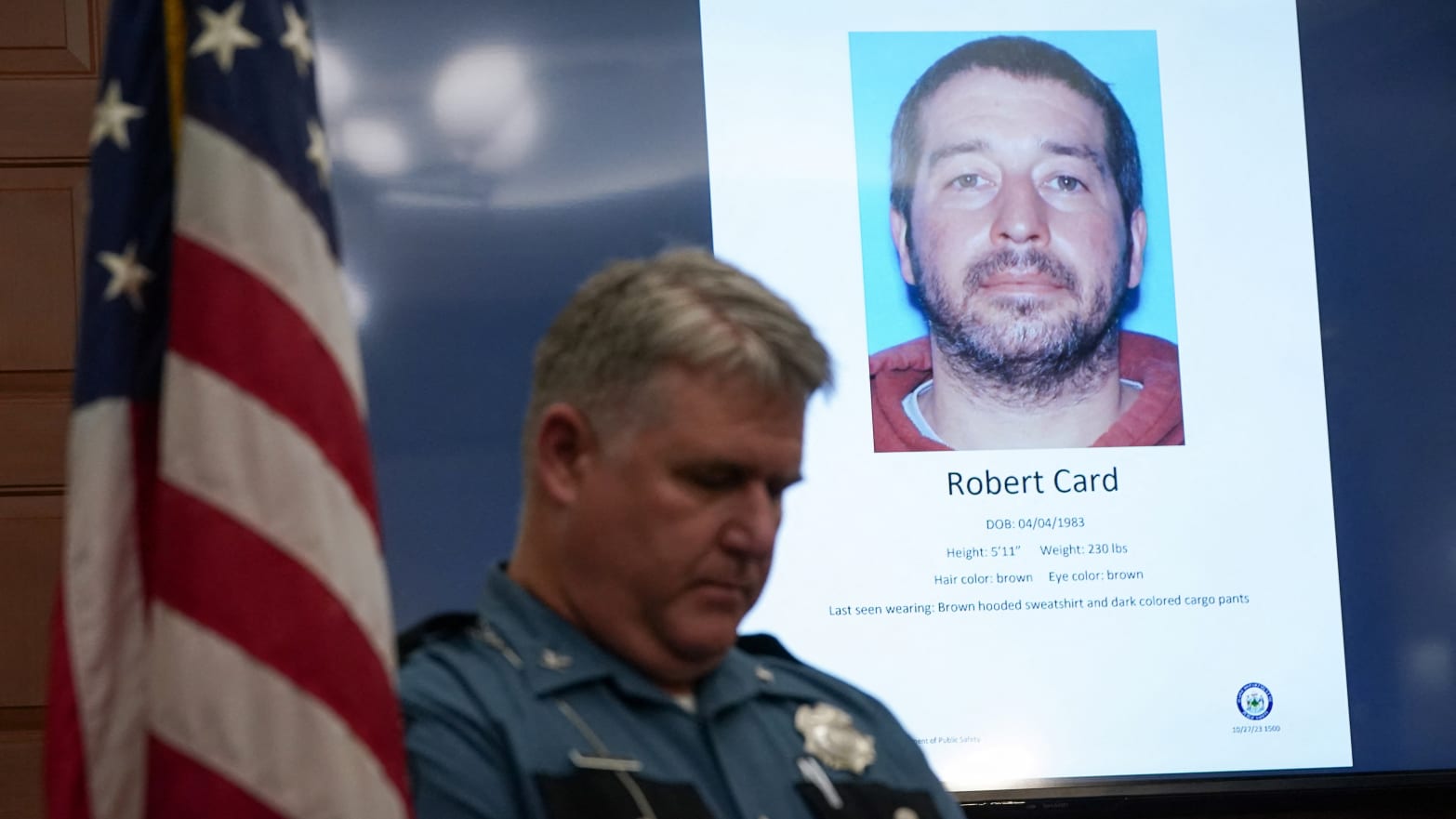 A police officer stands next to a screen displaying the picture of the suspected shooter, during a press conference following the deadly mass shooting, at City Hall in Lewiston, Maine.