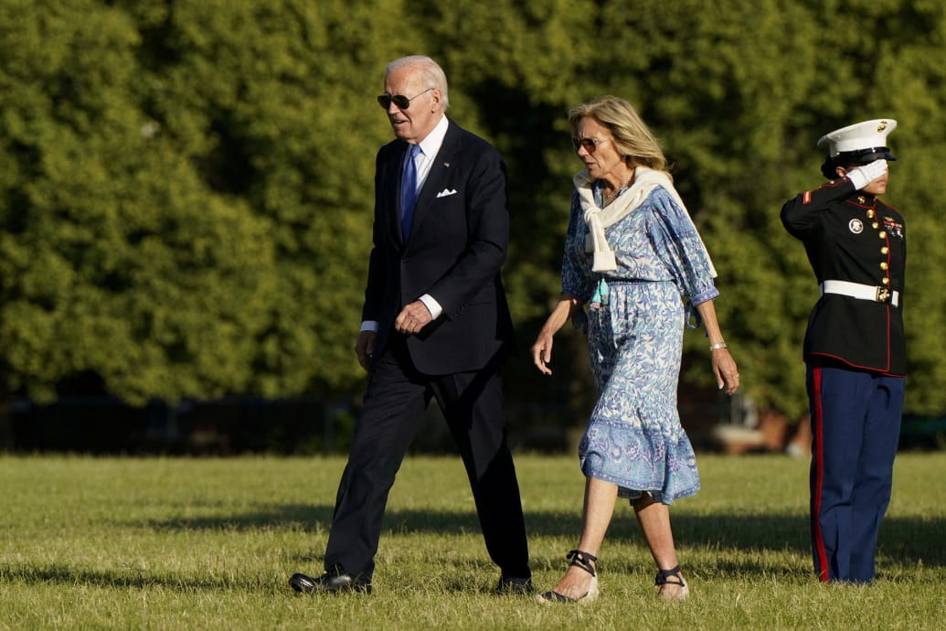 Jill and Joe Biden walking across grass at the White House in front of a saluting Marine