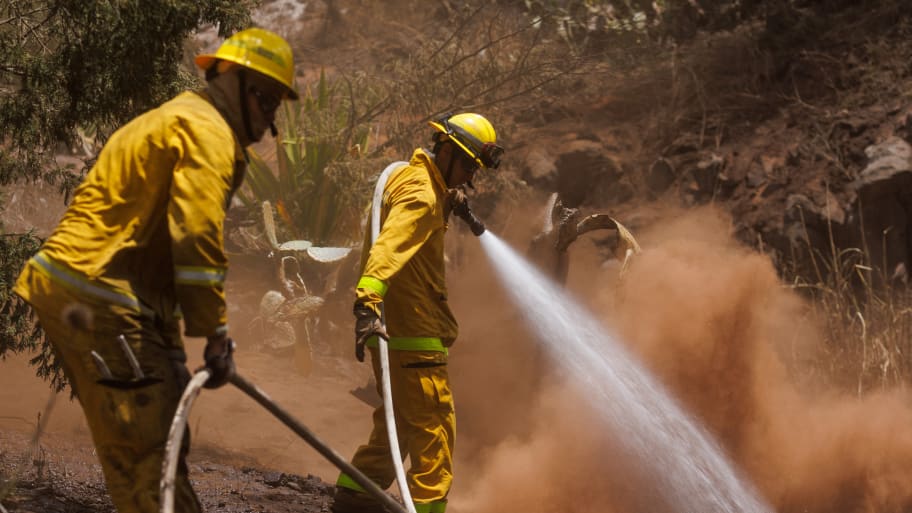 Maui County firefighters fight flare-up fires on Maui island. A delay in receiving state permission to use water streams for firegithers has drawn  criticism for possibly thwarting firefighters efforts to subdue the blaze.