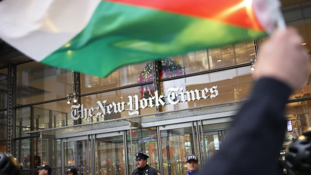 A Palestinian flag being waved in front of New York Times building.
