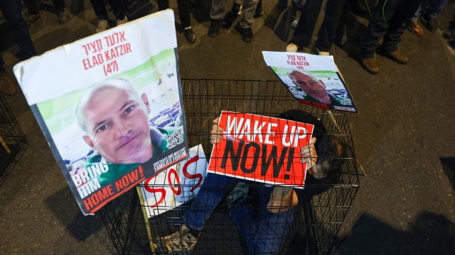 A man sits in a cage with portraits of 47-year-old Israeli hostage Elad Katzir as relatives and supporters of Israeli hostages held in Gaza since the October 7 attacks by Hamas militants, stage a demonstration in Tel Aviv, on March 26