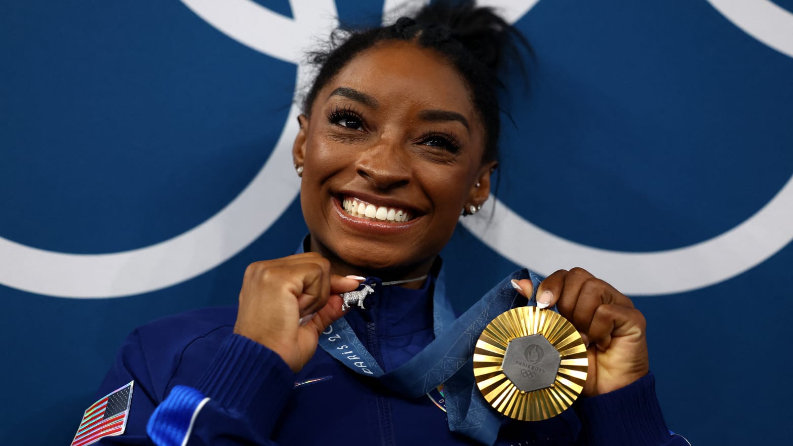 Simone Biles holds a goat necklace and her gold medal while smiling