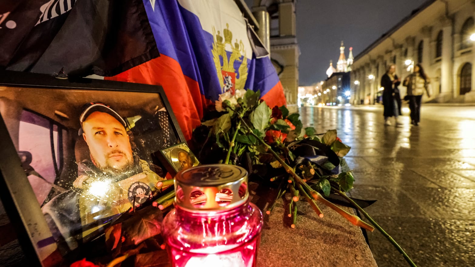 People walk past a portrait of Russian military blogger Vladlen Tatarsky, who was killed in a cafe explosion, with St. Basil’s Cathedral in the background in Moscow, Russia, April 4, 2023.