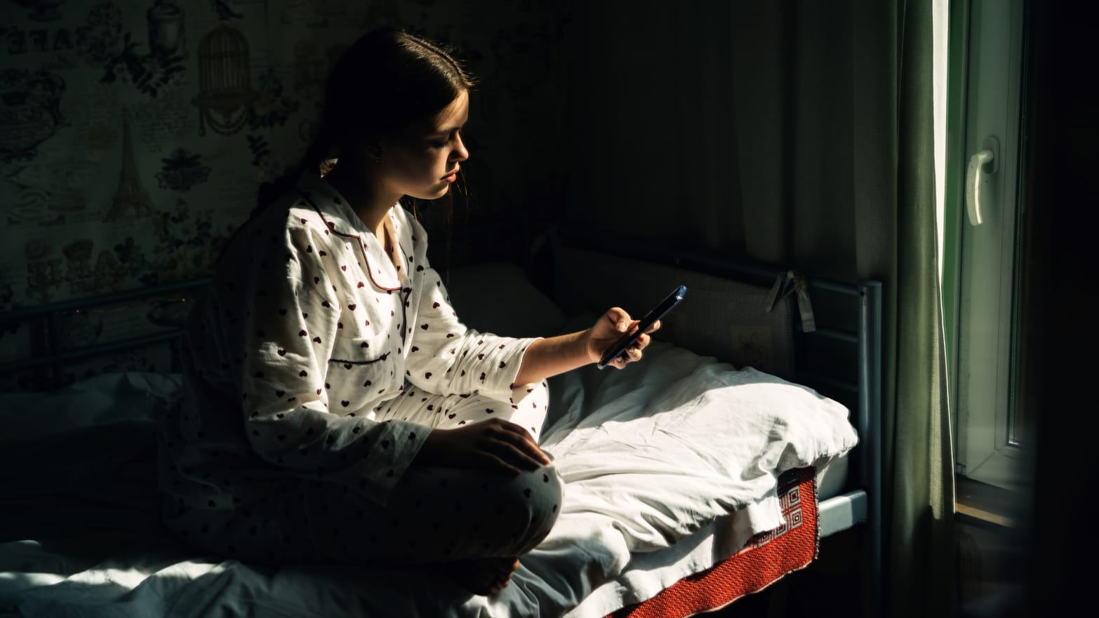 Portrait of a teenage girl with mobile phone sitting by the window in the village house. Concept of depression, loneliness, problems of adolescence