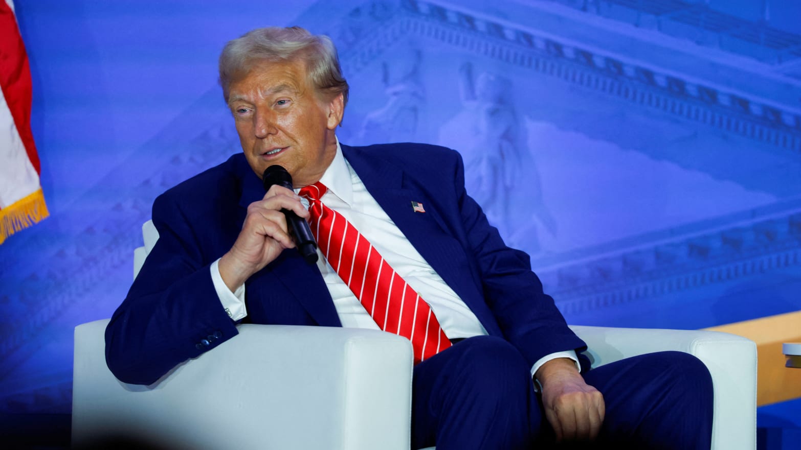 Donald Trump speaks on stage while sitting down.