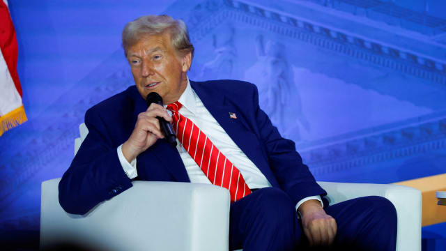 Donald Trump speaks on stage while sitting down.