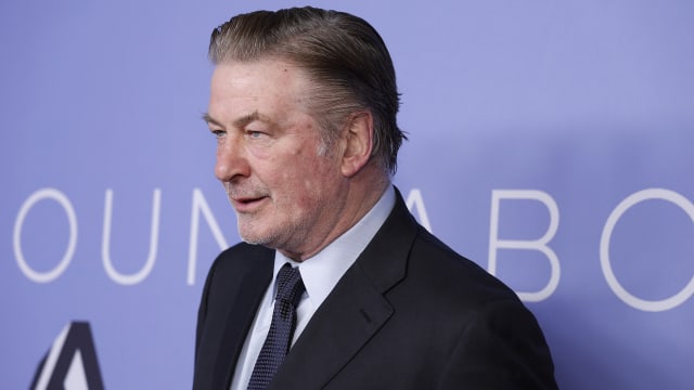 Alec Baldwin, wearing a suit and tie, stares forward at an event.