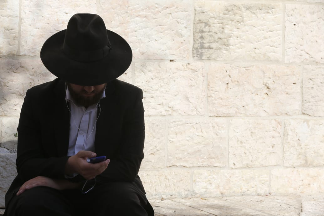 An orthodox jew outside of the Wailing Wall browses a cellphone