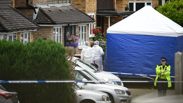 Forensic officers stand beside the police tent as a police officer surveys the scene in Ashlyn Close