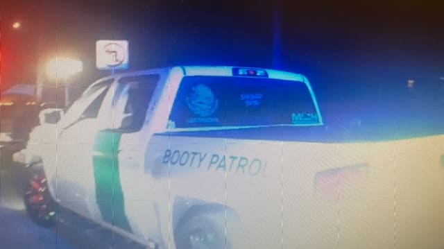 A white truck with the words “booty patrol” on it getting pulled over by a cop.