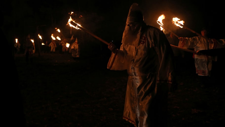 Ku Klux Klan members wearing white cloaks and hold torches.