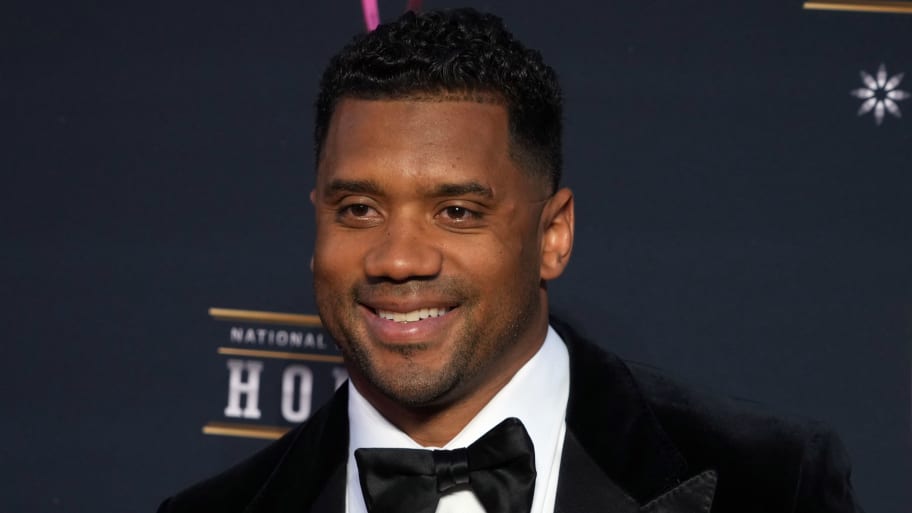Russell Wilson smiles on a red carpet.