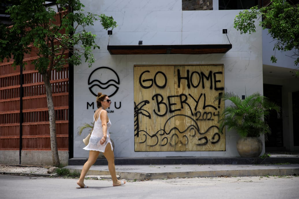 A woman walks in front of a sign saying "Go Home Beryl!"