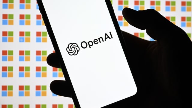 A photo illustration of the OpenAI logo displayed on a mobile phone screen in front of a repeating image of the Microsoft logo.