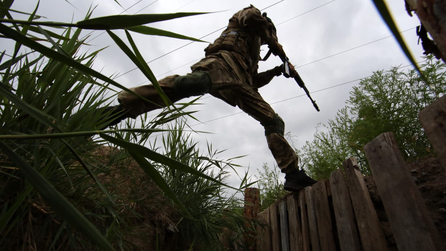 An armed National Guard serviceman jumps across a trench outside Kharkiv in Ukraine. 