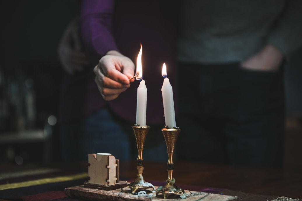 A hand lighting two shabbat candles.