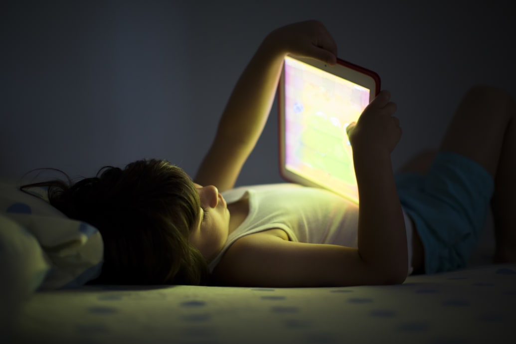 A child laying on bed staring into an iPad