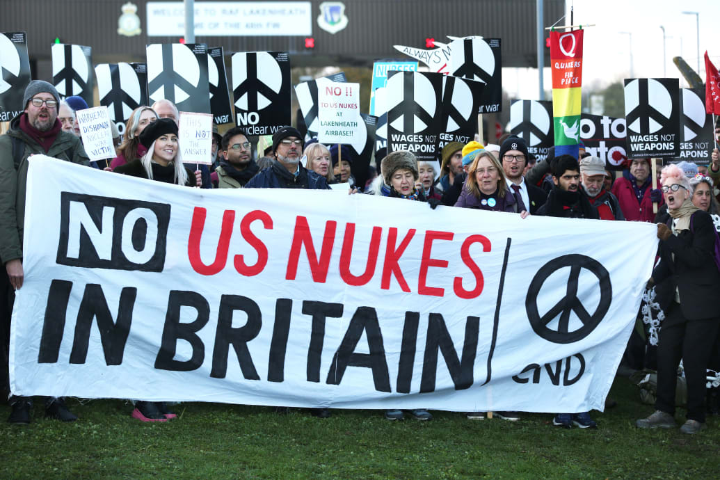 A photograph of protesters gather outside the air force base behind a large 'No Nukes in Britain' banner on November 19, 2022 in Lakenheath, England.