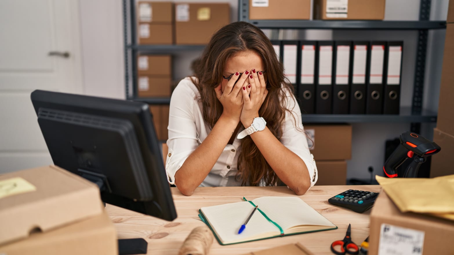 Young hispanic woman working at small business ecommerce with sad expression covering face with hands while crying. 