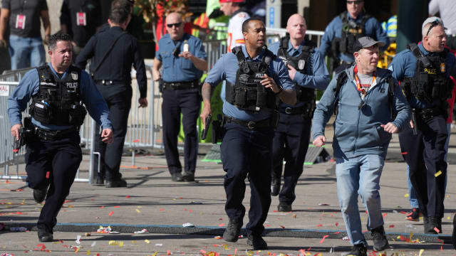 Uniformed officers, with guns drawn, run to the scene of a shooting at a parade in Kansas City. 