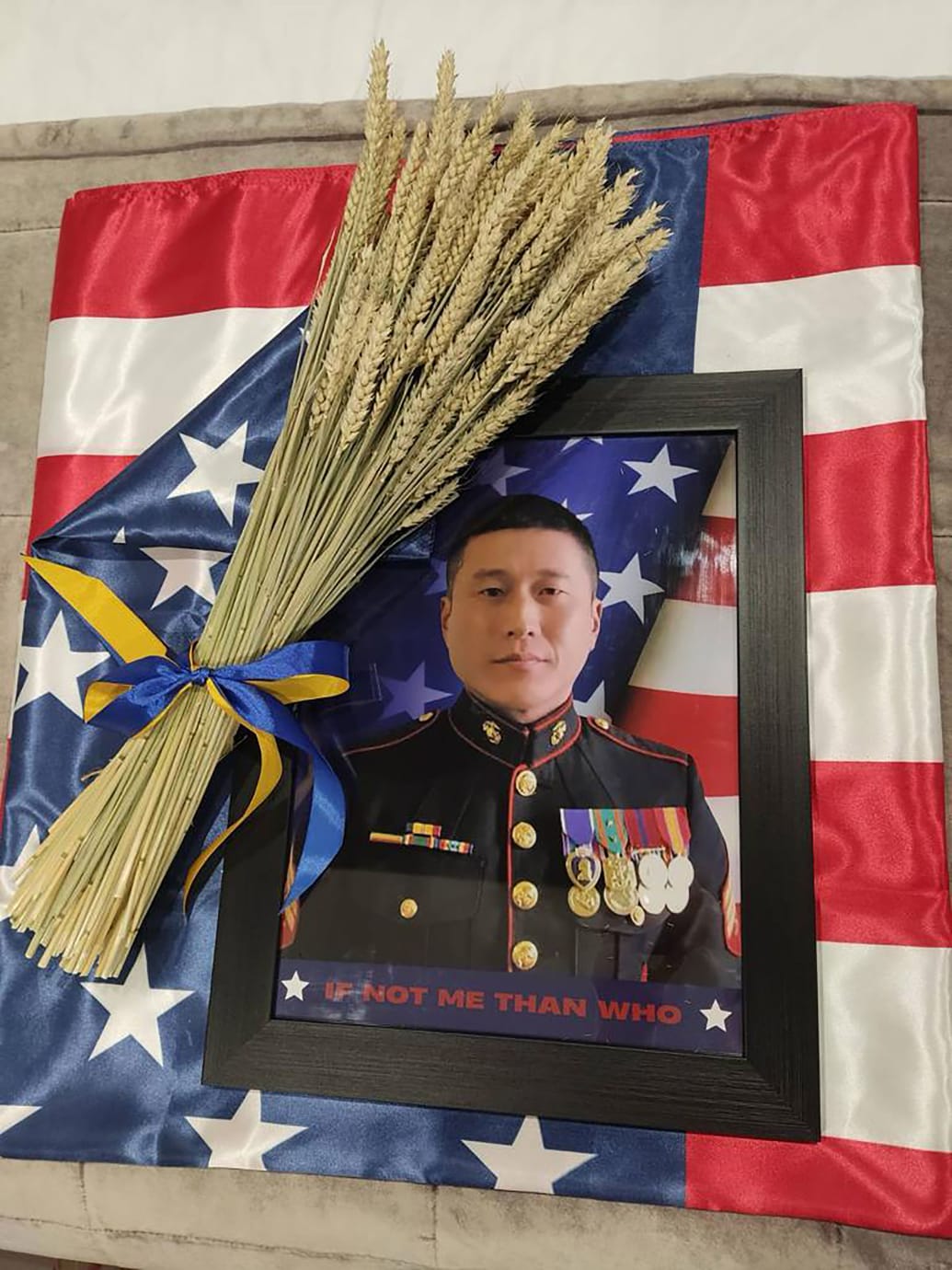 One photo shows a photo of Grady Kurpasi in his military uniform, atop an American flag.  On it lies a bundle of wheat, tied together in Ukrainian blue and yellow. 