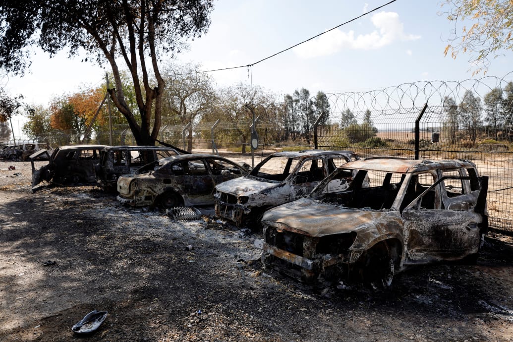 Burnt cars sit in a line in front of a barbed wire fence.