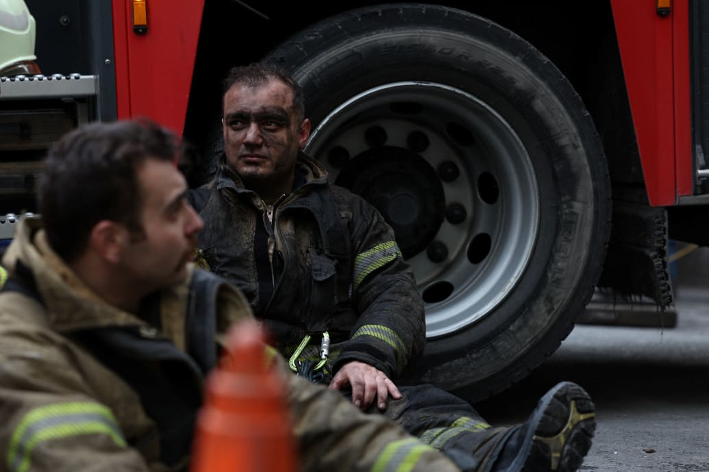 A firefighter sits down in uniform with his face blackened after fighting a fire.