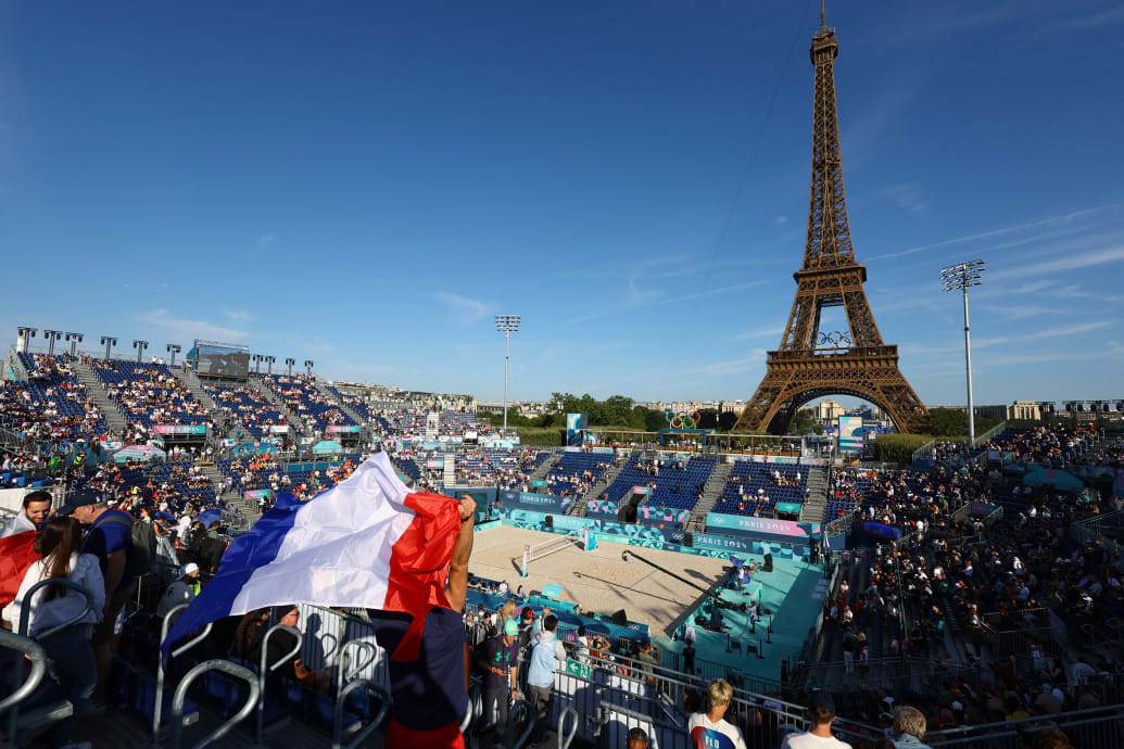 The Eiffel Tower Stadium with a beach volleyball stadium in front packed spectators, one wrapped in a French flag.