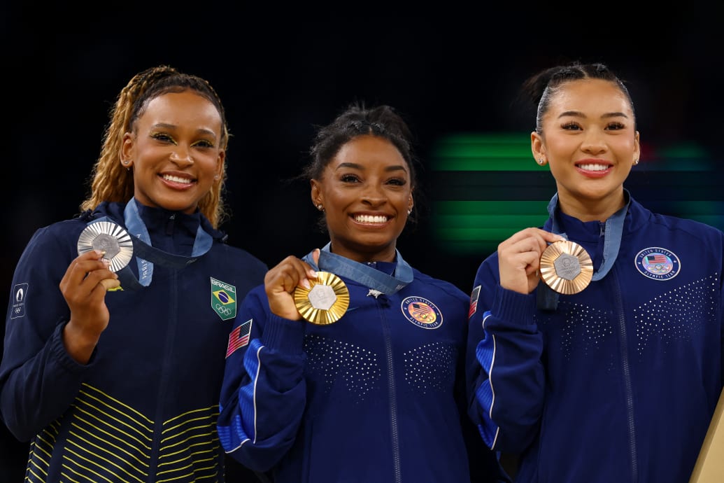 Simone Biles, Rebeca Andrade, and Sunisa Lee pose together.