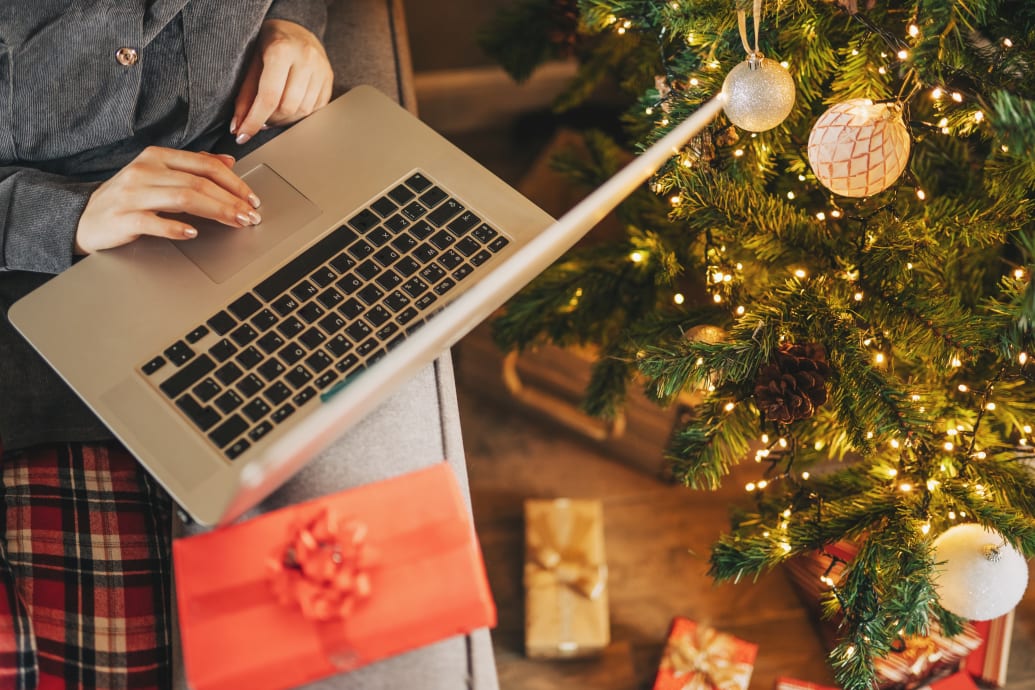 "Close up of woman hands with, gifts, coffee cup and laptop. Online shopping at Christmas holidays. Freelance girl woking from home office. Female typing at notebook computer. Christmas moments."