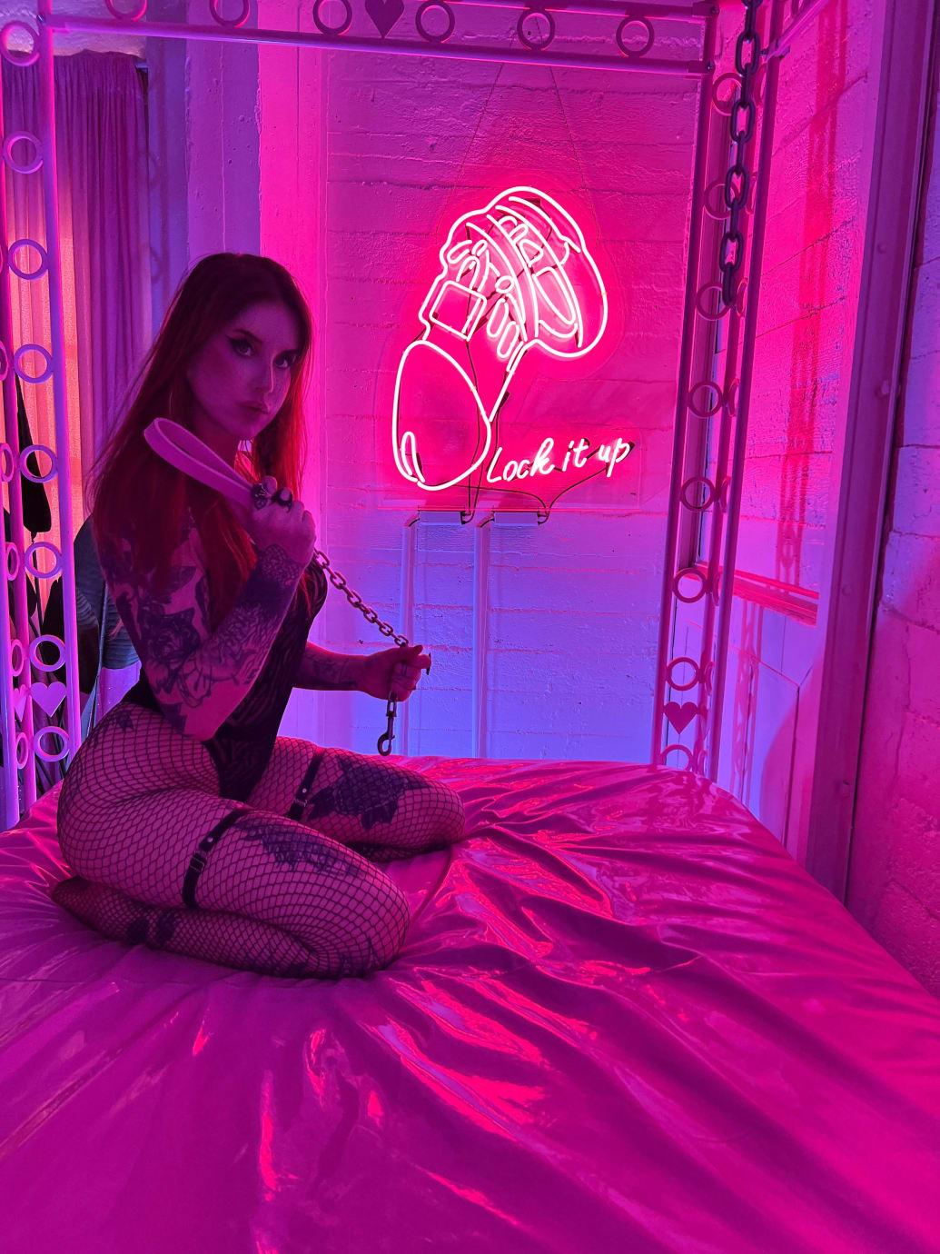 Photograph of Dominatrix Rin in black lingerie on a bed with a neon sign behind her