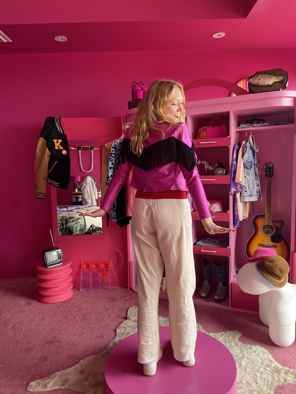 Fletcher trying on a pink Western jacket in a pink bedroom, in front of a wardrobe.