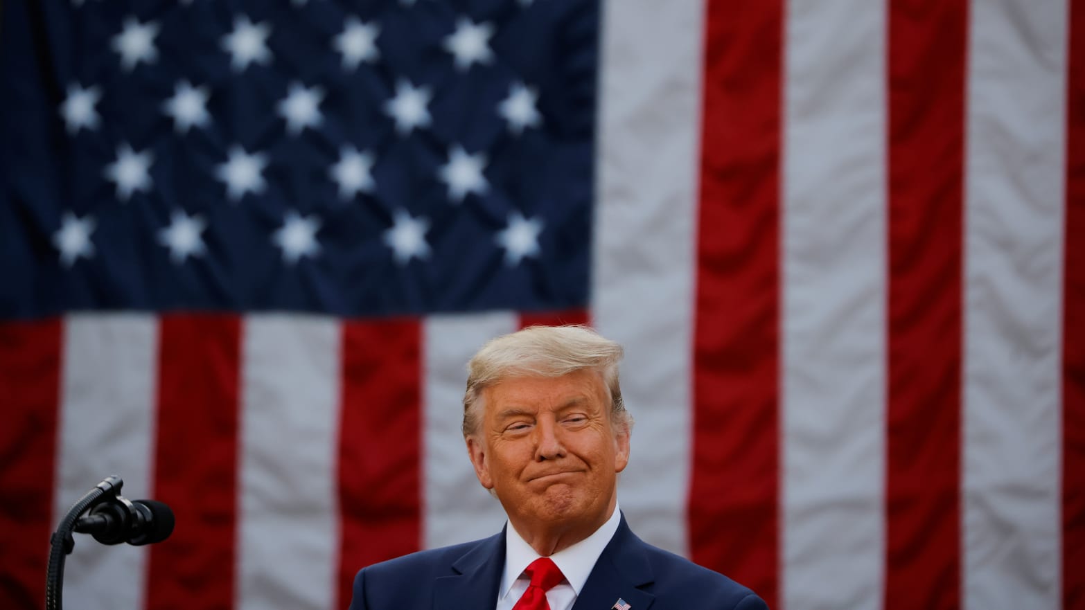 Donald Trump stands in front of a massive American flag.