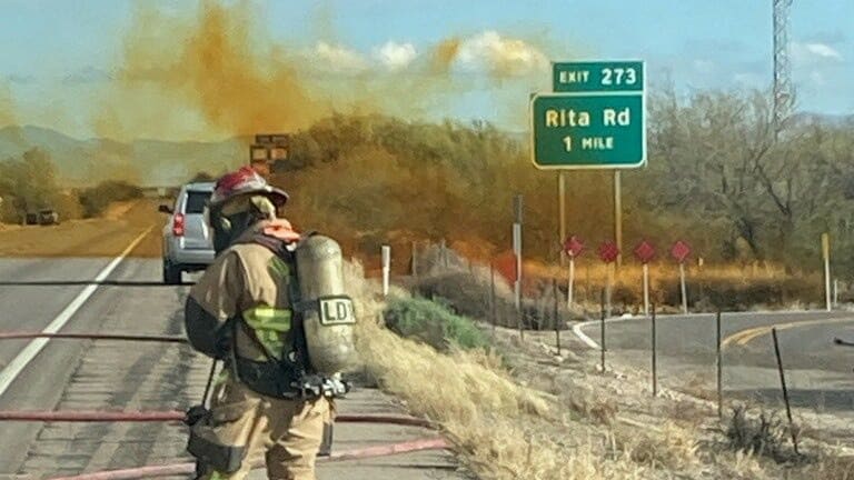 A firefighter works as an overturned truck spews orange smoke in the background at I-10 Highway in Tucson, Arizona, U.S., February 14, 2023. 