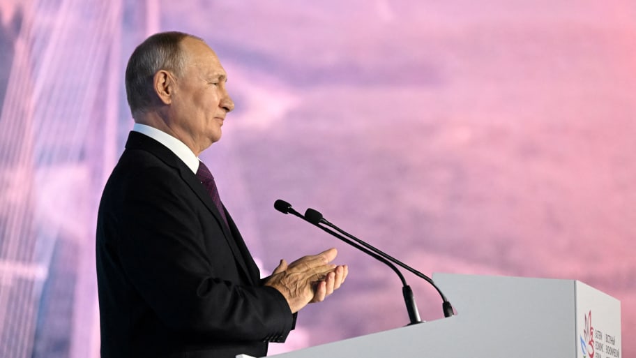 Russian President Vladimir Putin applauds at a conference before a pink backdrop.