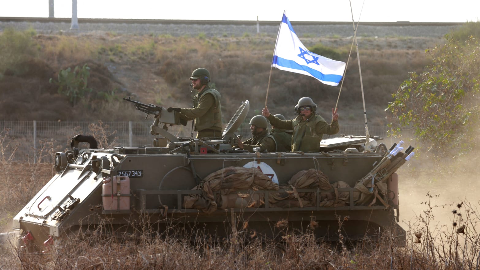 Israeli soldiers ride an armored vehicle topped with an Israeli flag. 