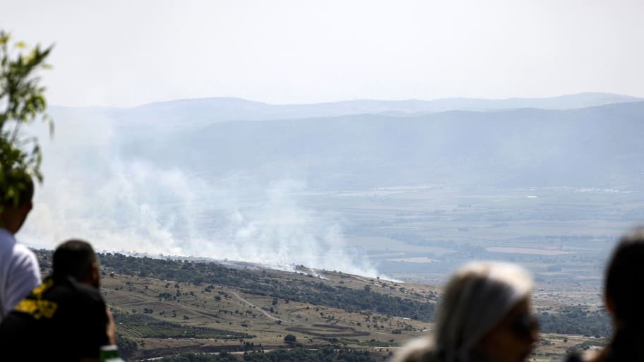 People watch as smoke rises at the site of a rocket strike from Lebanon on the Israel-annexed Golan Heights on May 17, 2024, amid ongoing cross-border clashes between Israeli troops and Hezbollah fighters.