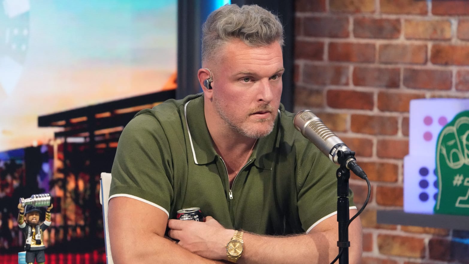Pat McAfee sits in a green polo while sitting in front of a microphone for his show.