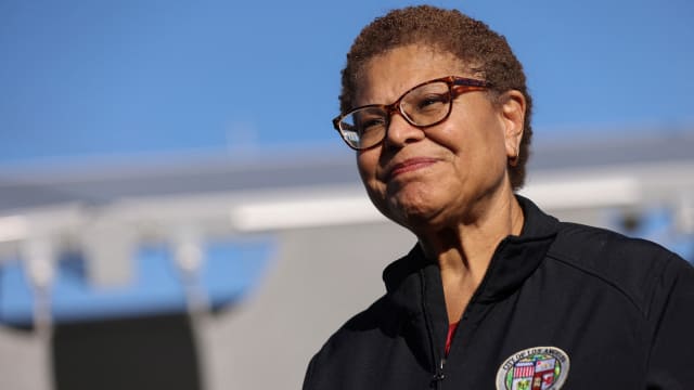 Karen Bass, wearing glasses, smiles while photographed at a press event outside.