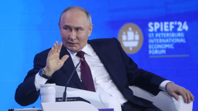 Russian President Vladimir Putin speaks while sitting in a chair with his hand raised up at the Saint Petersburg International Economic Forum.