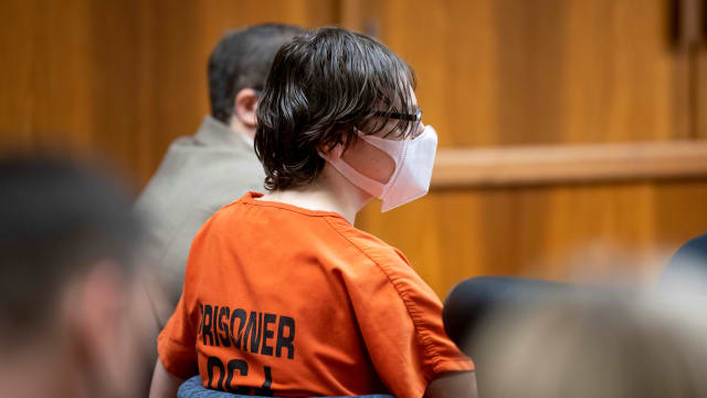 Ethan Crumbley, wearing a mask and an orange prison jumpsuit, stares forward in court.