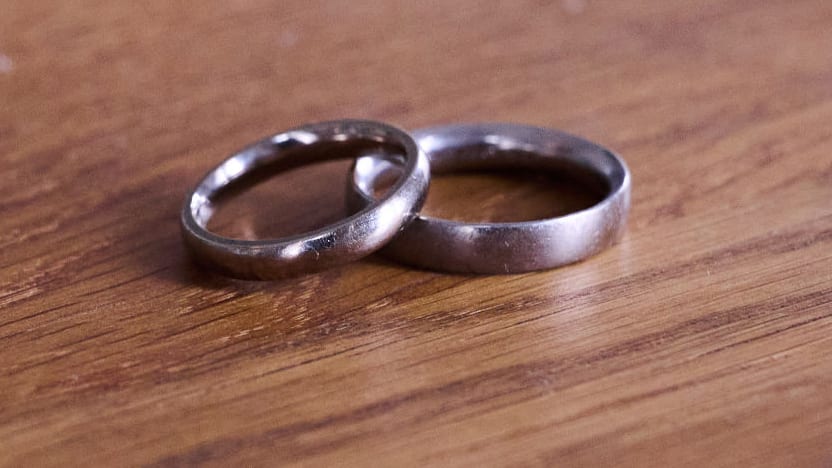 A pair of wedding rings lie on a wooden table.